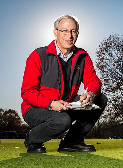 Bruce Clarke kneeling on turf with a clipboard and a pen in his hands.