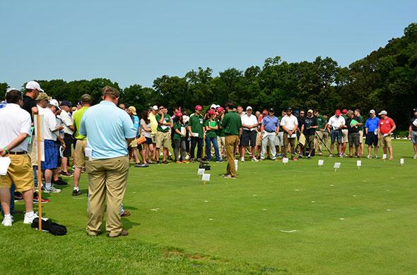 A large group of people of a turf plot, listening to a speaker.